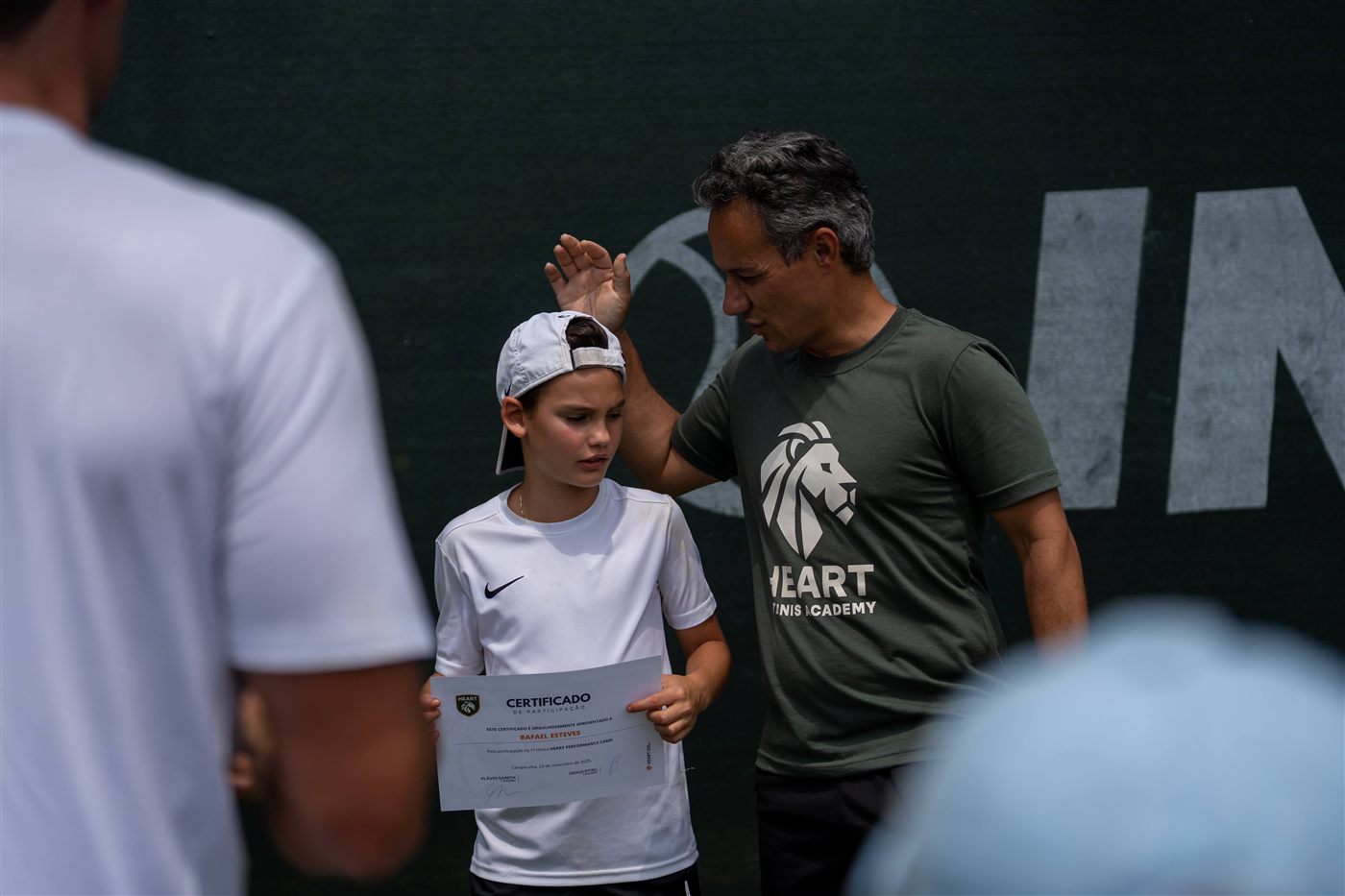 Diogo com a mão na cabeça de um jovem aluno segurando certificado